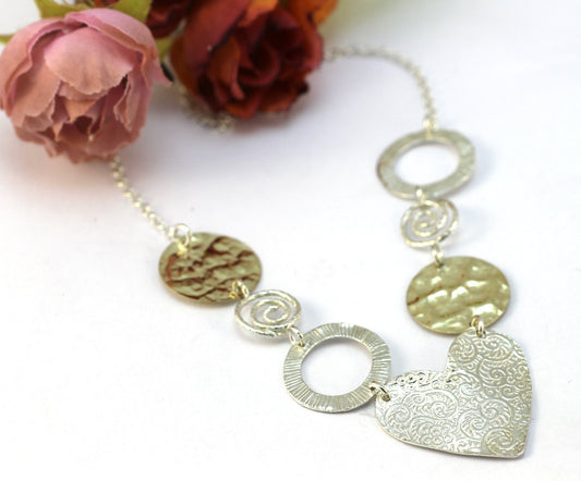 שרשרת משולבת כסף וגולדפילד עם תליון לב ואלמנטים בטקסטורות מגוונות
